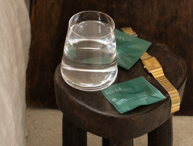 Men's pill sachet with gold watch and cup of water on a stool