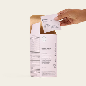 A hand lifts a daily sachet from an open box of Perelel 1st Trimester Prenatal Pack.