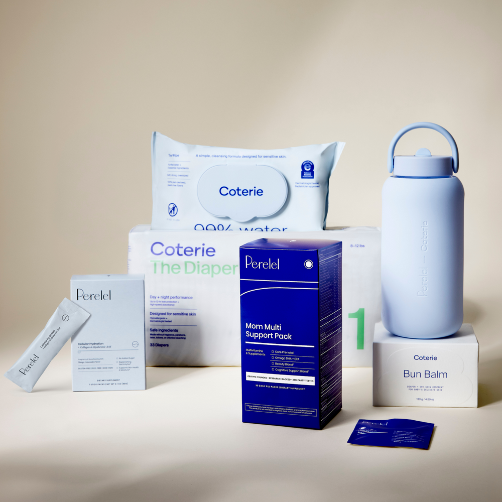 A coordinated set of Perelel and Coterie products arranged on a warm beige studio background: a large pack of wipes, a diaper box, a blue mom multi-support pack, a white bun balm box, cellular hydration box and travel stick, and a pale blue bottle.