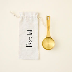 Gold measuring spoon next to a white drawstring bag with 'Perelel' branding on a beige background