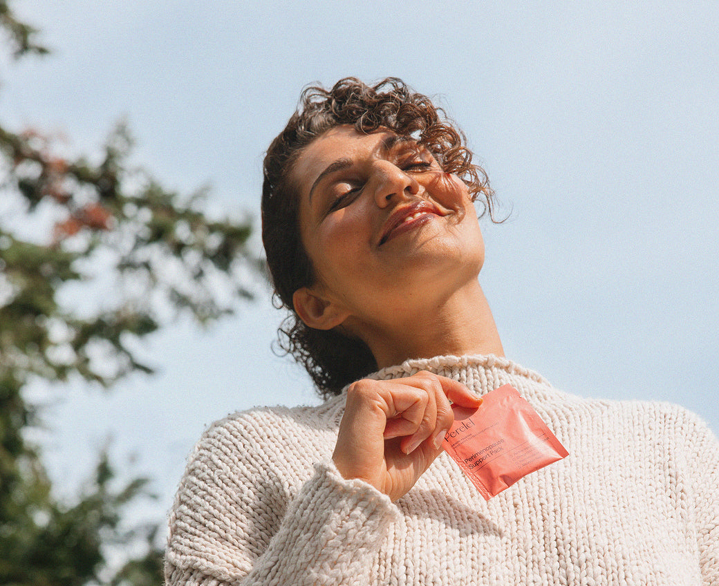 A person outdoors holds a coral Perelel daily sachet.