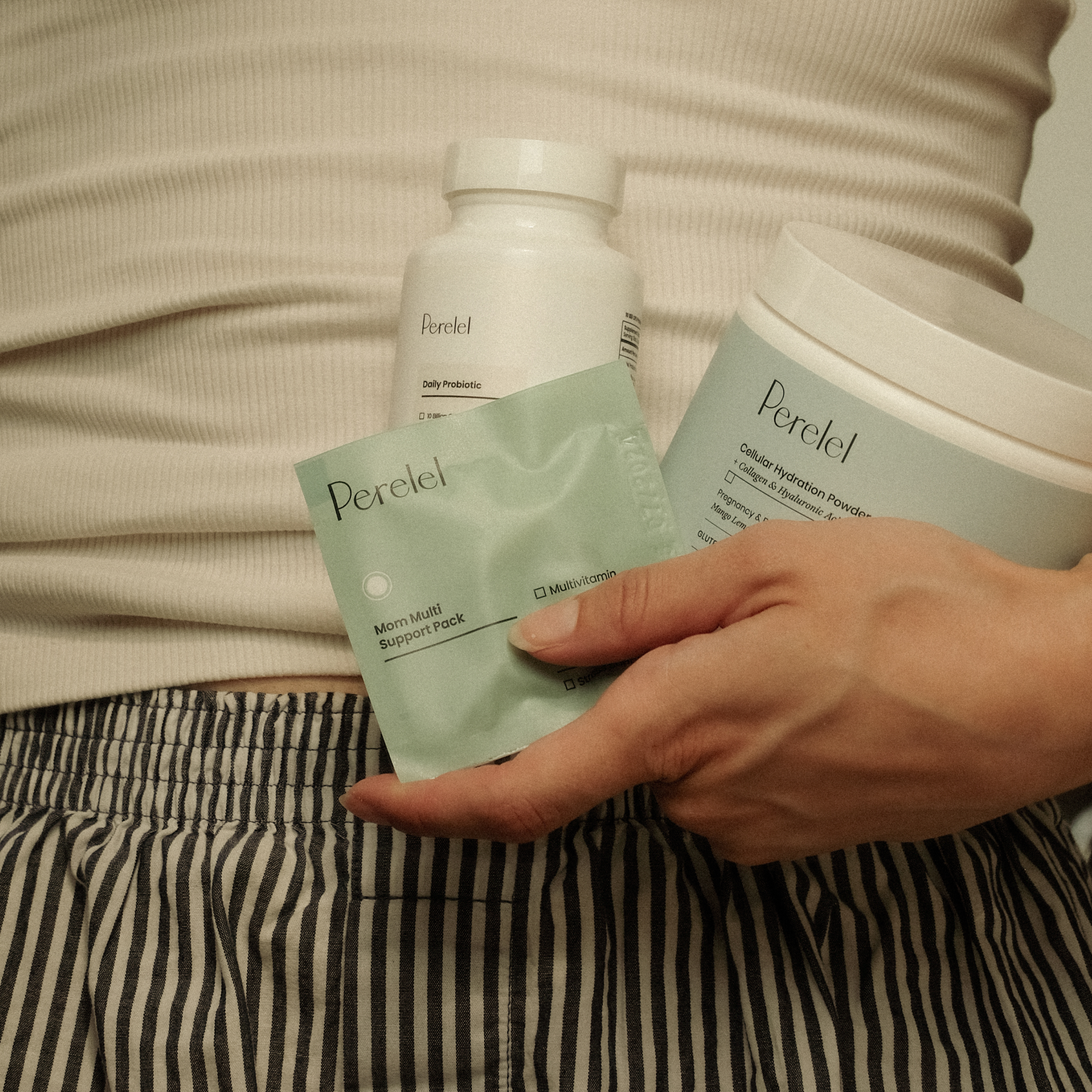 hand holding mom multi pill sachet with hydration powder tub and daily probiotic pill bottle