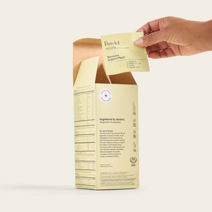 A hand lifts a daily sachet from an open box of Perelel Recovery Support Pack.